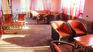 A room with wicker furniture, including chairs and a table, and a stone floor. - Amboseli Getaway Hotel (Kimana)