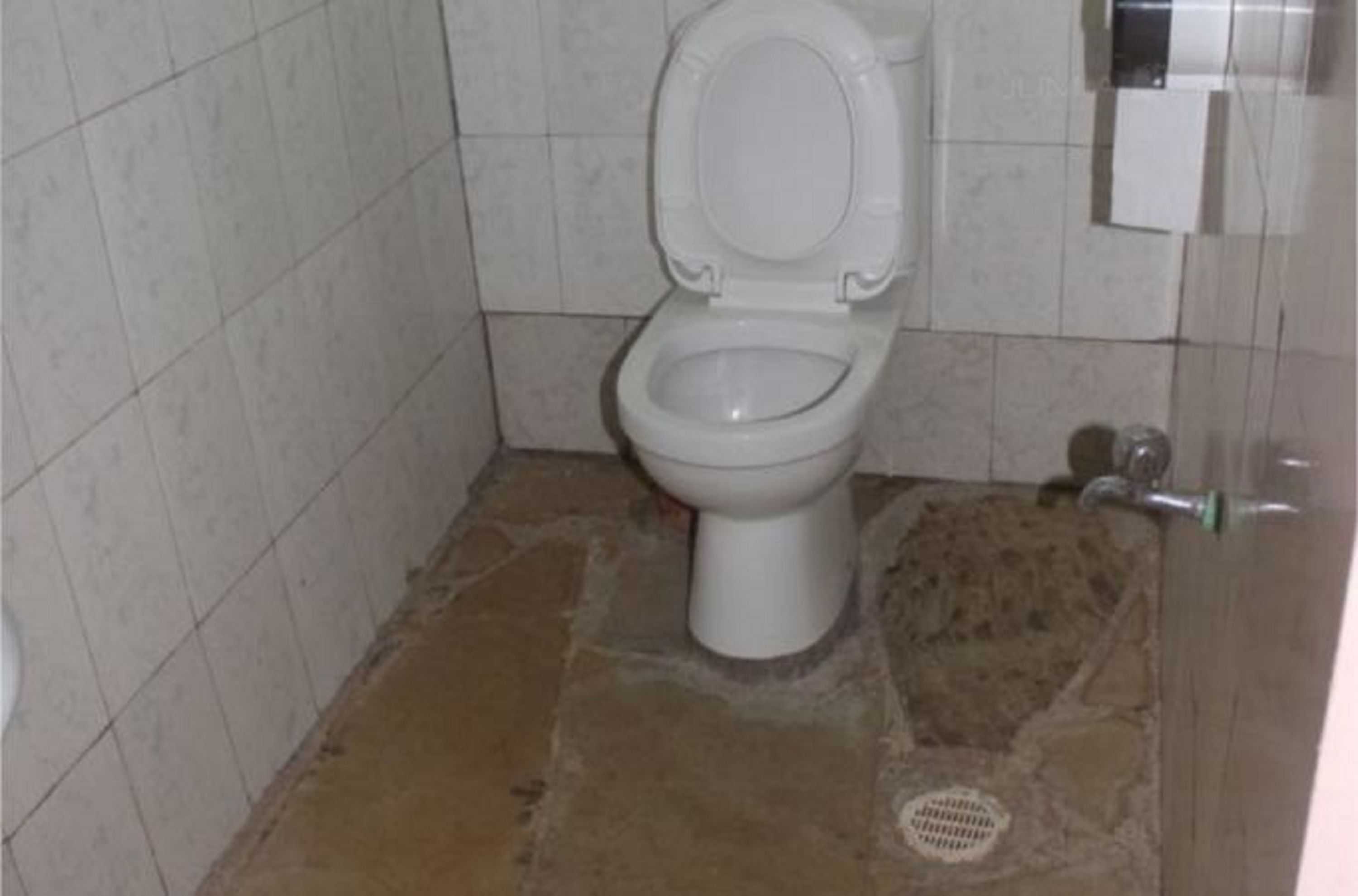 Un baño pequeño, con azulejos, que incluye inodoro y desagüe visible.