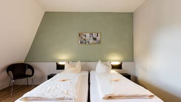 Een hotelkamer met twee enkele bedden, een zwarte stoel, een kleine tafel en een aan de muur hangend schilderij.