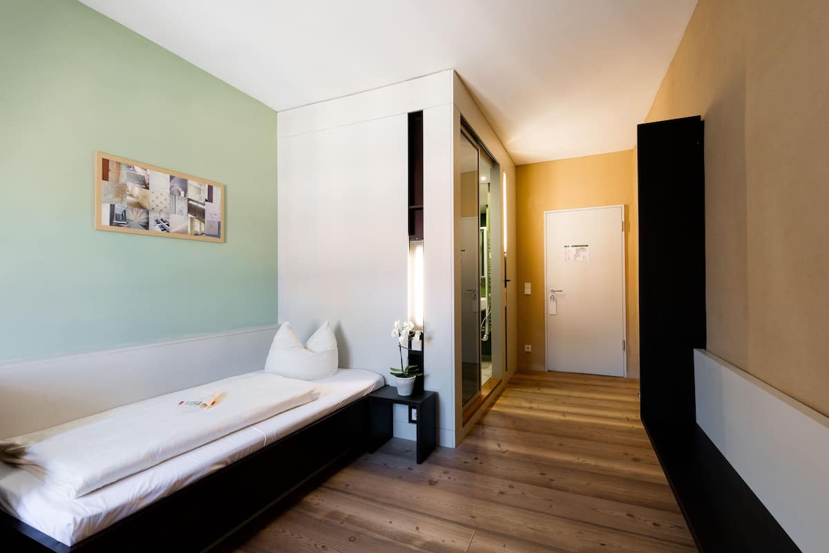 A modern bedroom with a bed, a small bedside table, a wall-mounted artwork, and a sliding door leading to a bathroom.