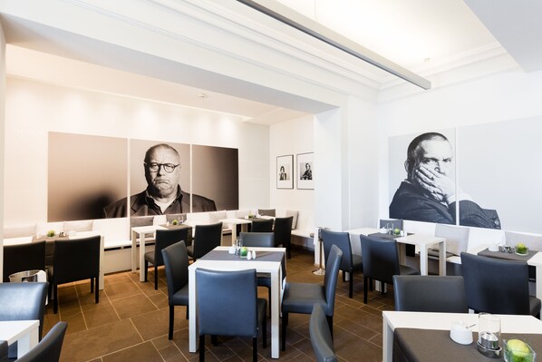 Un comedor moderno con mesas y sillas, techo blanco y obras de arte en las paredes.