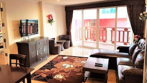 Ein Wohnzimmer mit Sofa, Couchtisch, Fernseher und einer Schiebetür, die auf einen Balkon führt.