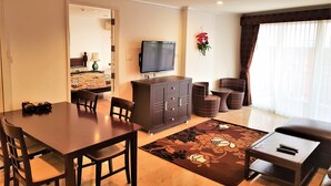 Ein Wohnzimmer mit Esstisch, Stühlen, einer Couch, einem Fernseher und einem kleinen Tisch mit Fernbedienungen.