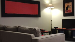 Una sala moderna con un cuadro abstracto grande, un sofá, una lámpara de pie, un televisor de pantalla plana y una mesita con un cuenco.