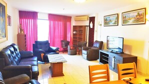 A living room with a sofa, chairs, a TV, and a bookshelf. - Sea View 1 bed Apartment (Pattaya)