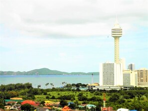 A high-rise building with a prominent tower, surrounded by greenery and a body of water.