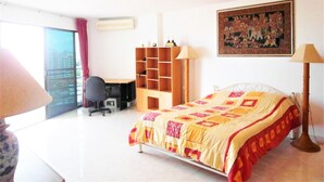 A hotel room with a bed, desk, chair, bookshelf, and a large window. - Sea View 1 bed Apartment (Pattaya)