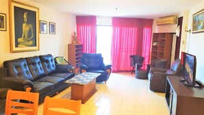 A living room with a black leather sofa, a blue armchair, a wooden coffee table, and a TV on a stand. - Sea View 1 bed Apartment (Pattaya)