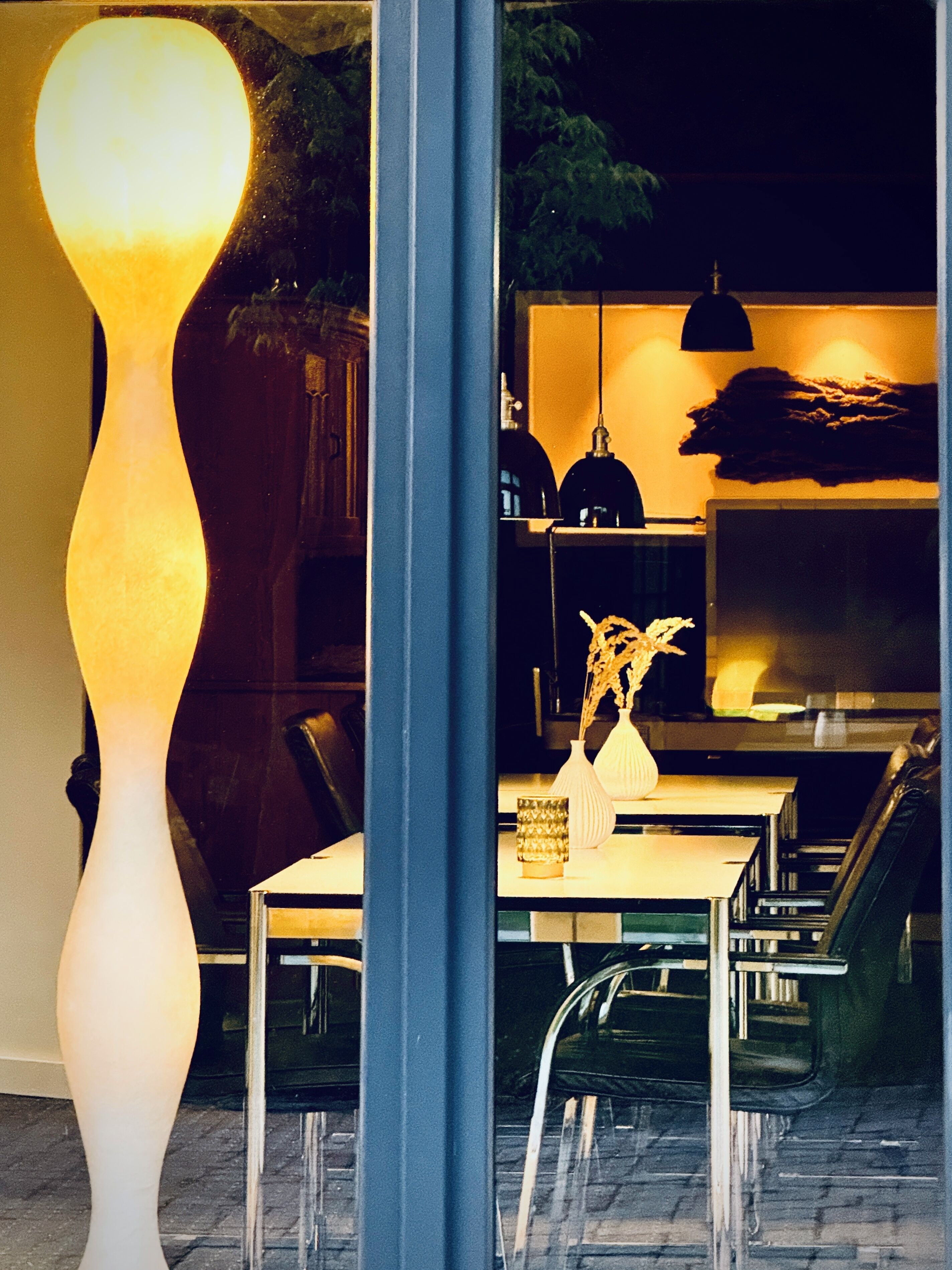 Ein modernes Interieur mit einer hohen, beleuchteten Skulptur, einem Essbereich mit Stühlen und Tisch sowie hängenden Pendelleuchten.