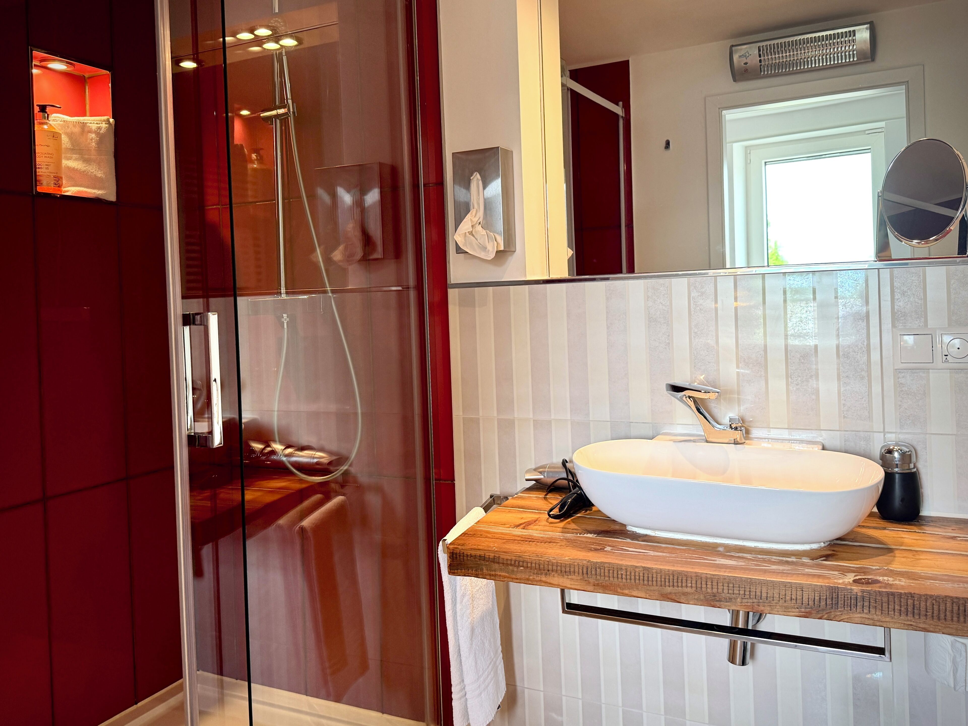 Un baño moderno con ducha de vidrio, lavamanos blanco y encimera de madera.