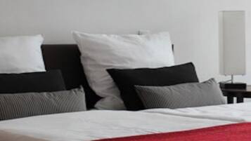 A bed with white and red bedding, a black headboard, and a nightstand with a lamp.