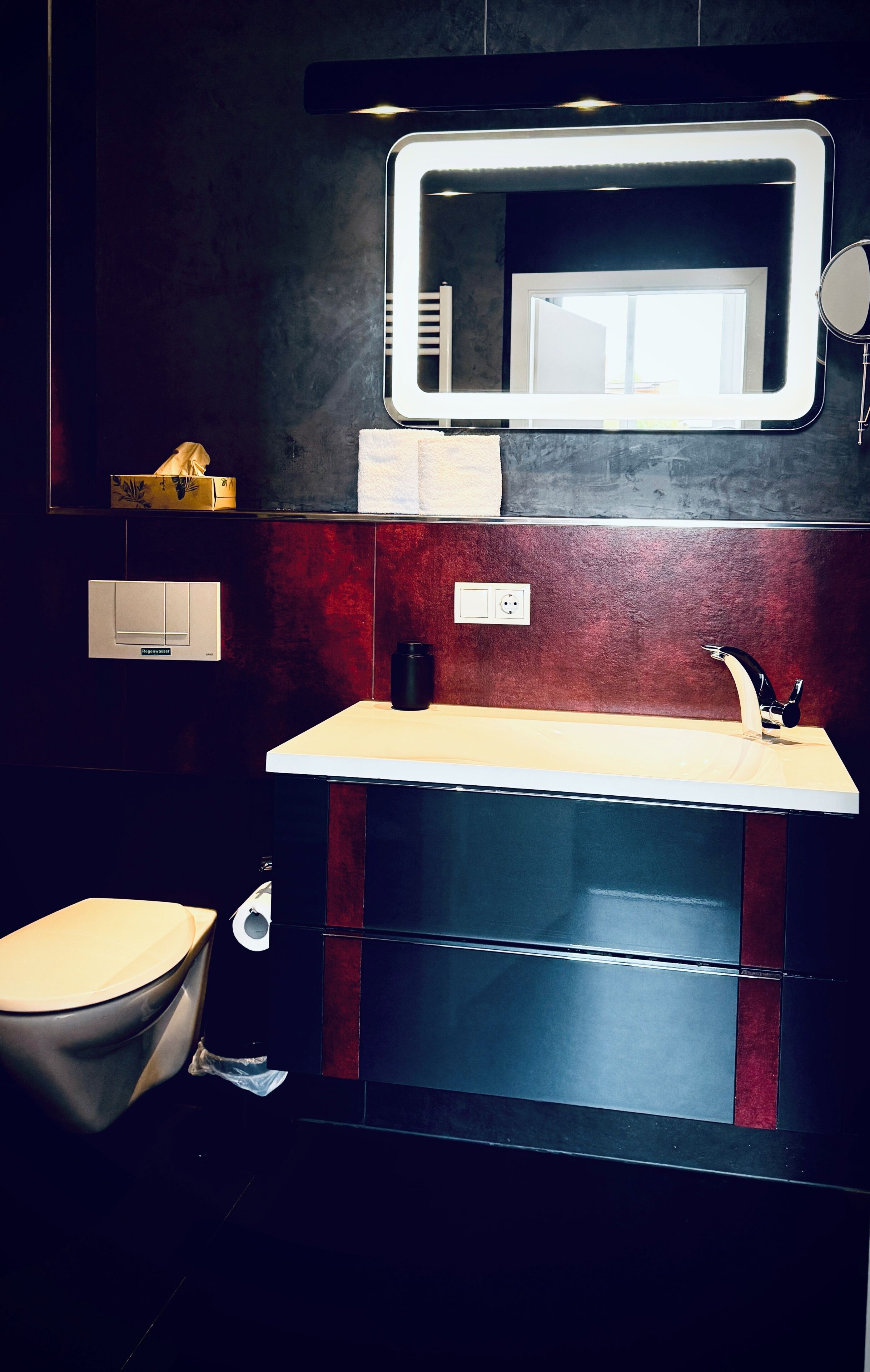 Un baño moderno con un espejo grande, un inodoro, un lavabo y un perchero para toallas.