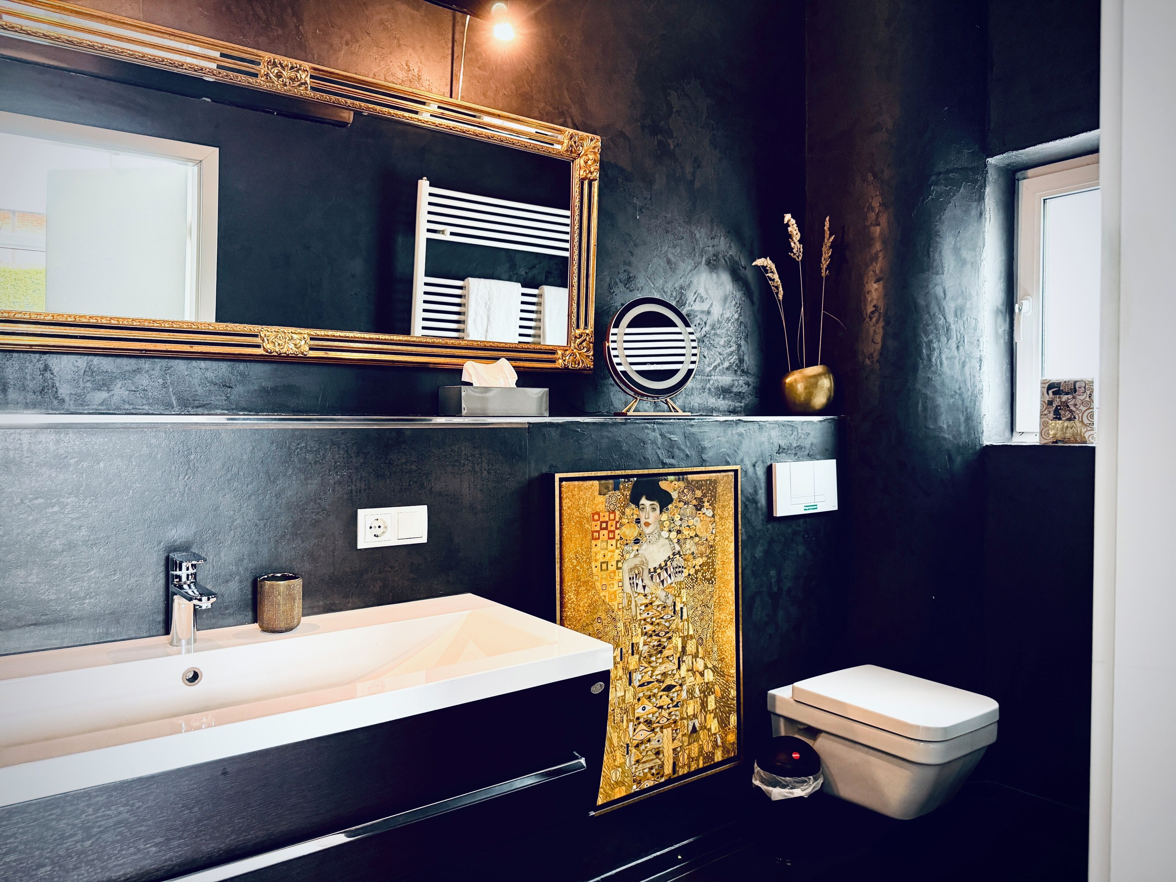 Une salle de bain moderne avec un grand miroir, un lavabo blanc, des toilettes et un tableau décoratif.