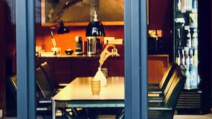 A dining area with a table, chairs, a lamp, and a refrigerator in the background. - Aparthotel Flughafen Leipzig (Schkeuditz)