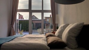 A bedroom with a bed, a lamp, and a view of the outside. - Aparthotel Flughafen Leipzig (Schkeuditz)