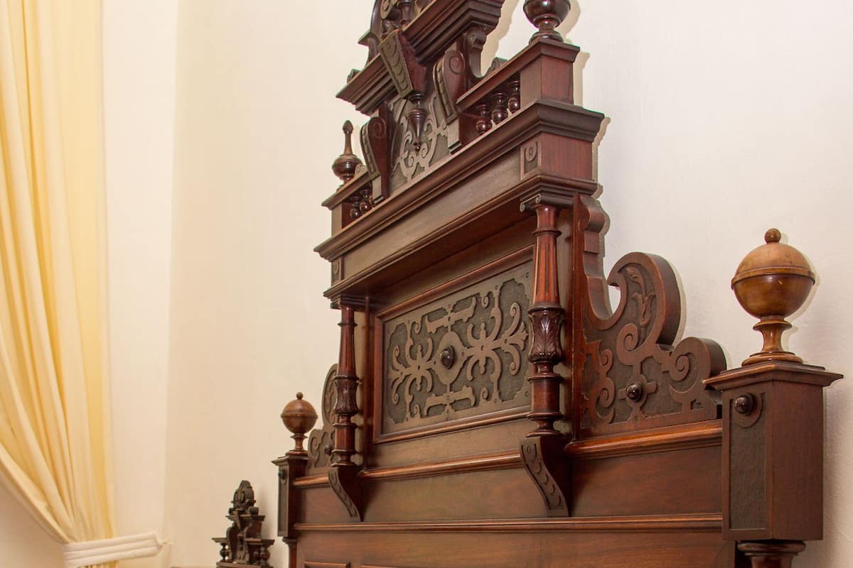 Un lit en bois avec une tête de lit sculptée, une table de chevet et une couvre-lit à motifs.