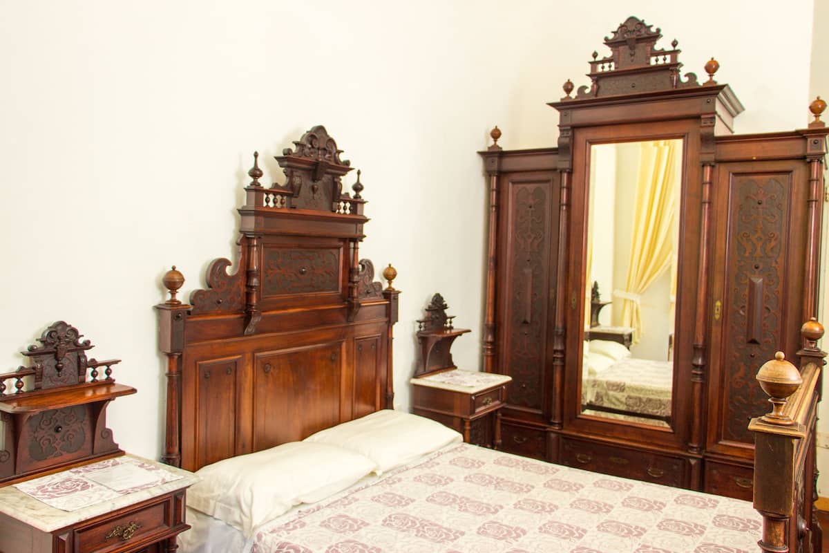 Une chambre à coucher traditionnelle en bois, dotée d’un grand miroir, d’un lit avec une literie à motifs et d’une table de chevet avec une lampe.