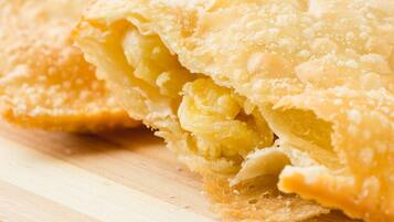 Um doce com crosta dourada, possivelmente uma torta ou pastel, sobre uma superfície de madeira.