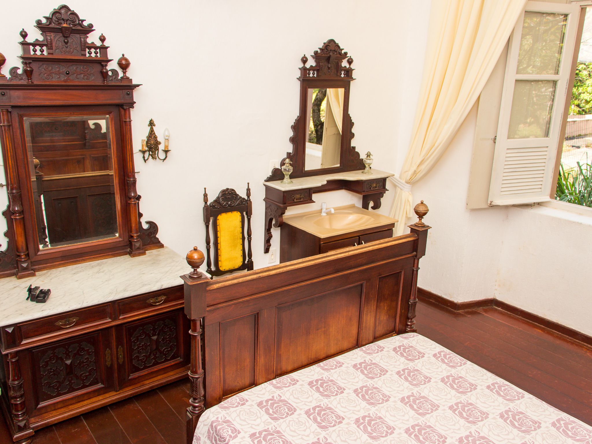A bedroom with a wooden bed, a dresser with a mirror, and a window with curtains.