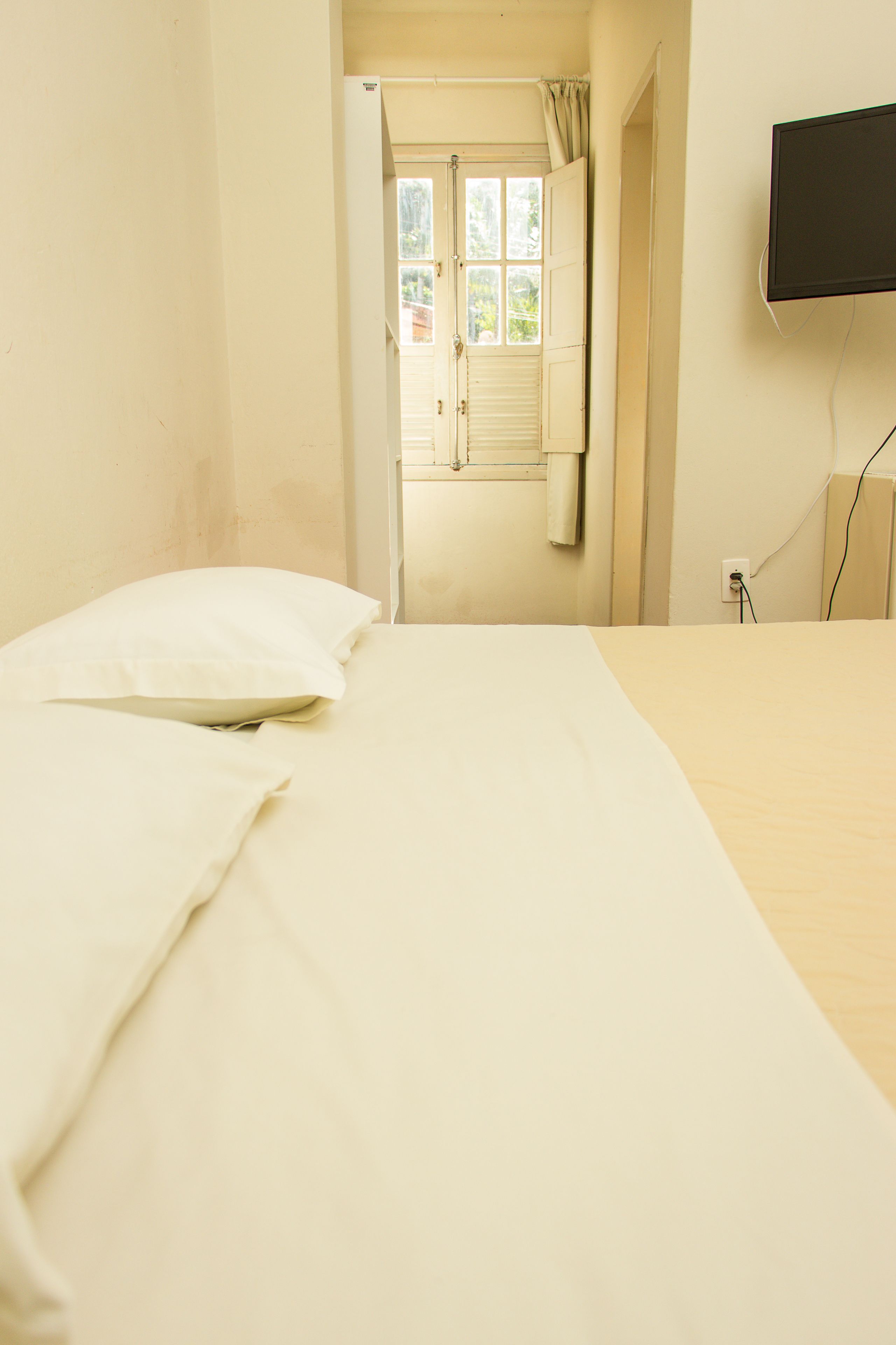 Une chambre à coucher avec un lit, un téléviseur fixé au mur et une fenêtre avec des rideaux.