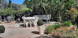 Un espace patio aménagé avec une table et des chaises, entouré d’un jardin où poussent différentes plantes et fleurs.