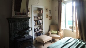 Une pièce avec un poêle ancien, un grand miroir, une bibliothèque, une chaise et une fenêtre avec des rideaux.