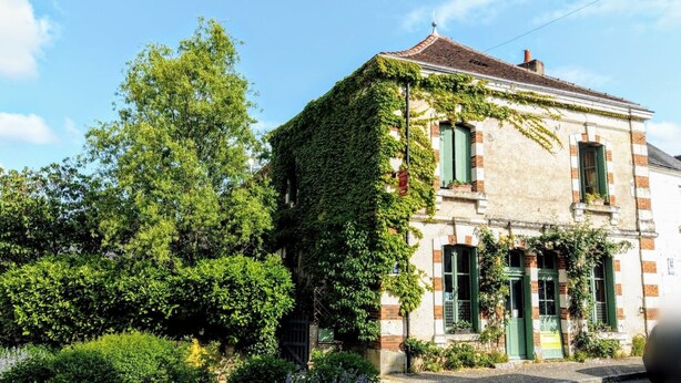 Un bâtiment historique aux murs recouverts de lierre, doté d’un toit traditionnel en tuiles et d’une porte verte.