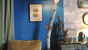 Une pièce avec un mur bleu, une chaise, une lampe et une petite table sur laquelle se trouvent des livres et une bouilloire.