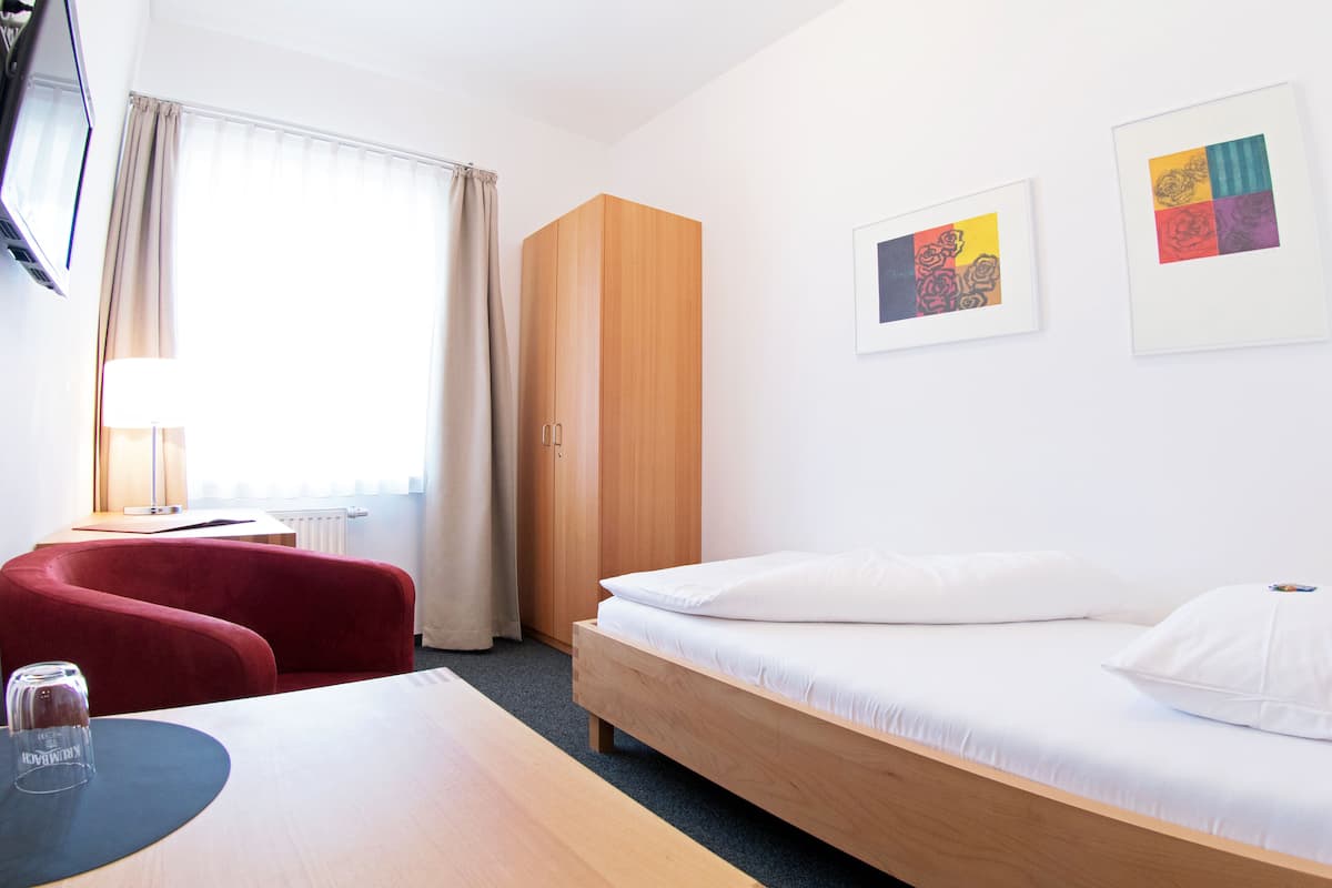 Ein Hotelzimmer mit Bett, Schreibtisch, Stuhl, Kleiderschrank und zwei Bildern an der Wand.