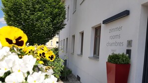 A narrow alley with a building labeled "zimmer rooms chambres" and a planter with greenery. - Ökölogisches Bildungszentrum Kultiviert (Wildpoldsried)