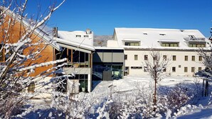 A modern building with large windows and a flat roof, surrounded by snow-covered ground and trees. - Ökölogisches Bildungszentrum Kultiviert (Wildpoldsried)