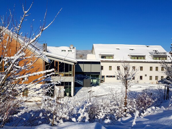 Un edificio moderno con amplios ventanales y techo plano, rodeado de nieve y árboles.
