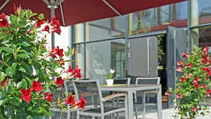 An outdoor seating area with a table and chairs, surrounded by potted plants with red flowers. - Ökölogisches Bildungszentrum Kultiviert (Wildpoldsried)