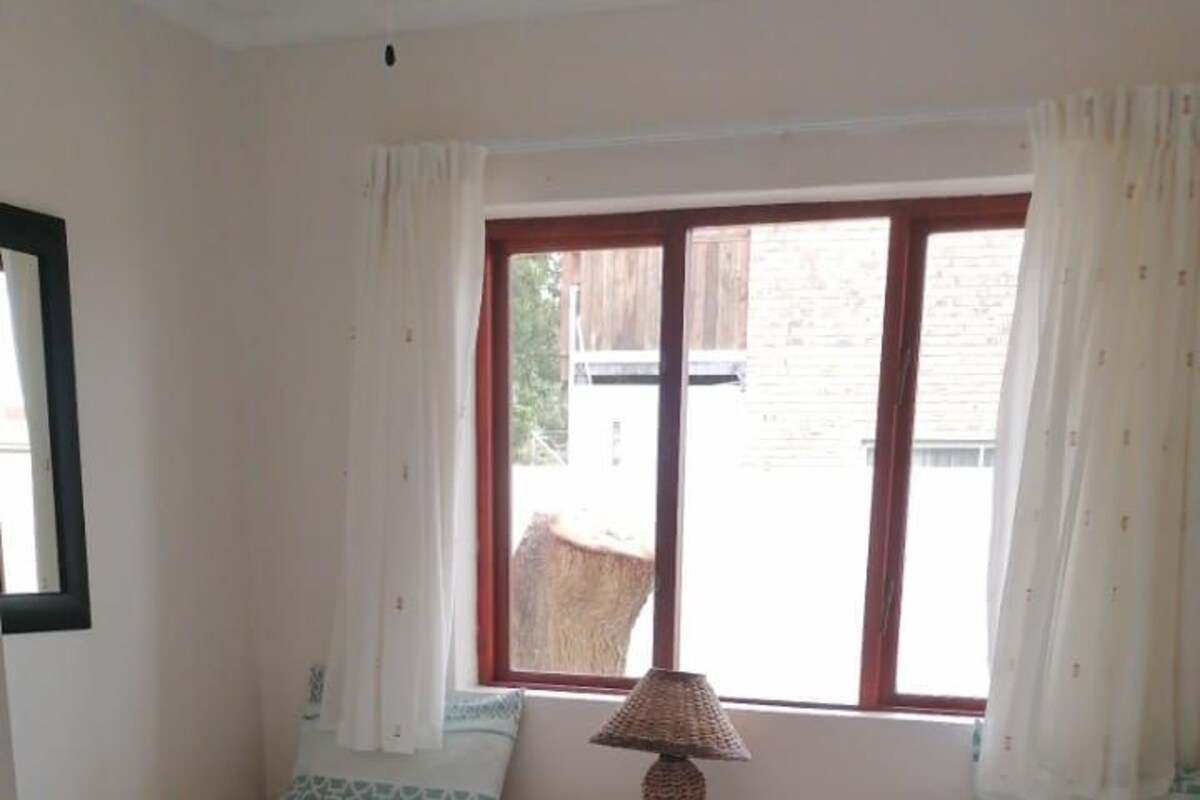 A small, clean room with two single beds, a nightstand, and a window with curtains.