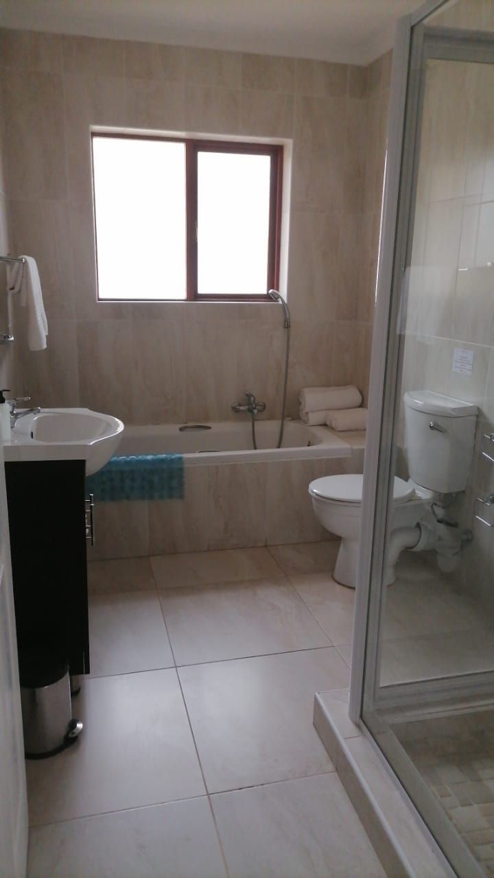 A bathroom with a bathtub, toilet, and sink. There is a window above the bathtub and a shower area to the right.