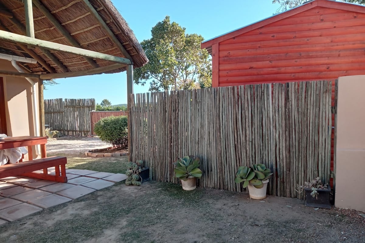 A patio with a wooden table and bench, a red shed, and a wooden fence.