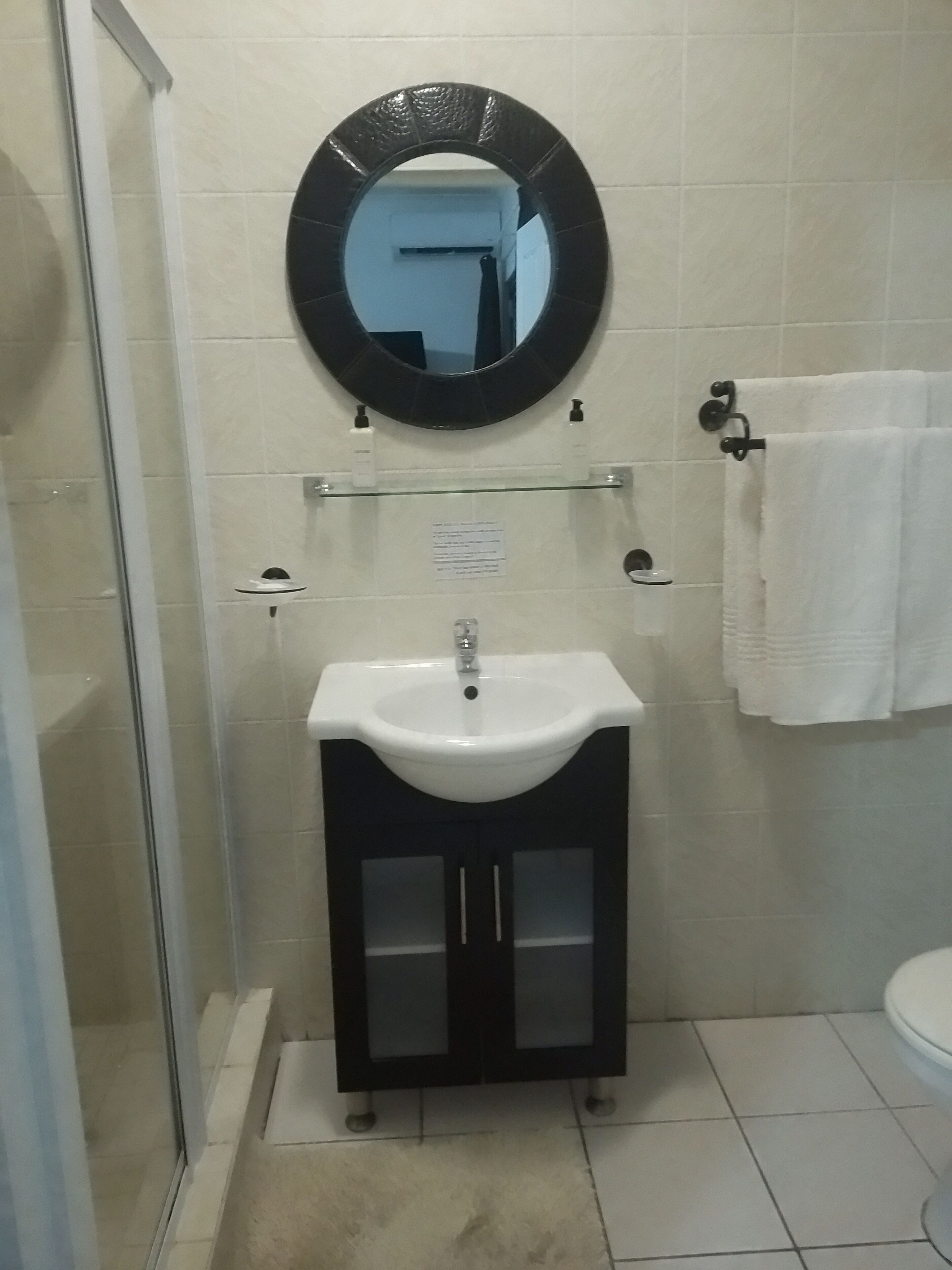 Un baño con un lavabo blanco, mueble negro y un espejo redondo.