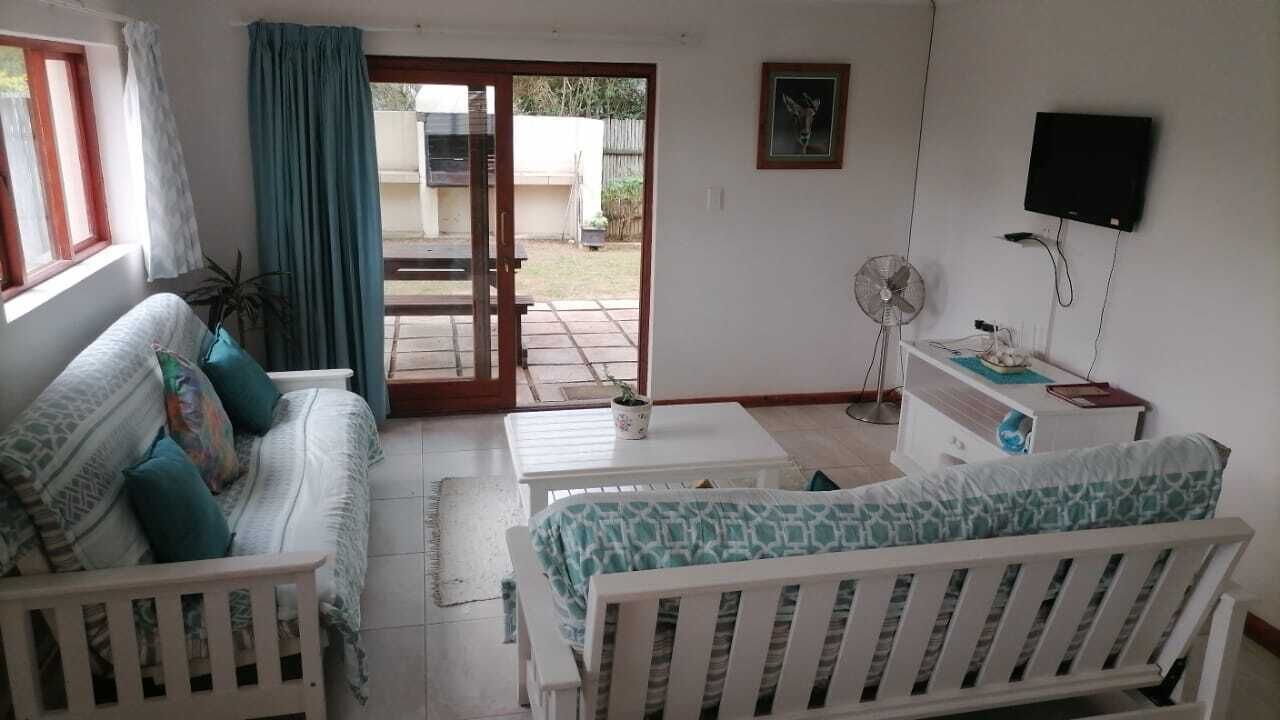 Une pièce comprenant un canapé, une table à manger, un téléviseur fixé au mur et une porte-fenêtre coulissante donnant sur un espace extérieur.