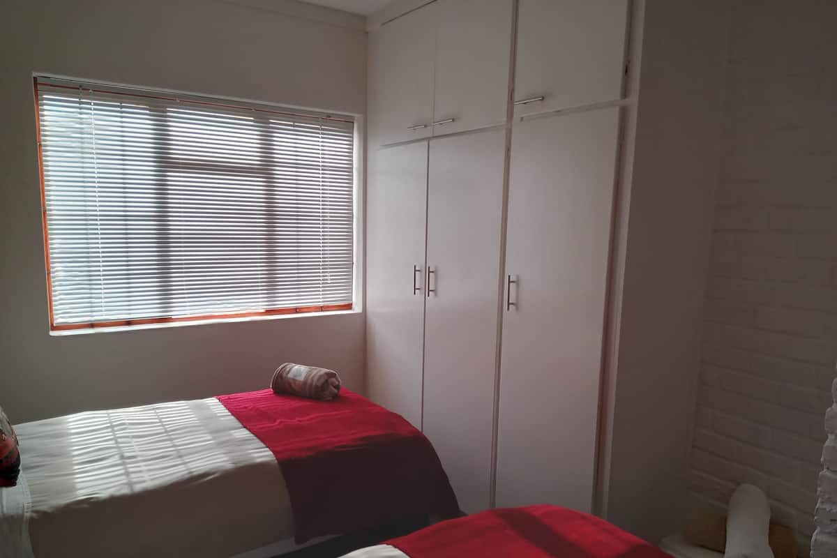 A bedroom with two beds, a window with blinds, and a wardrobe.