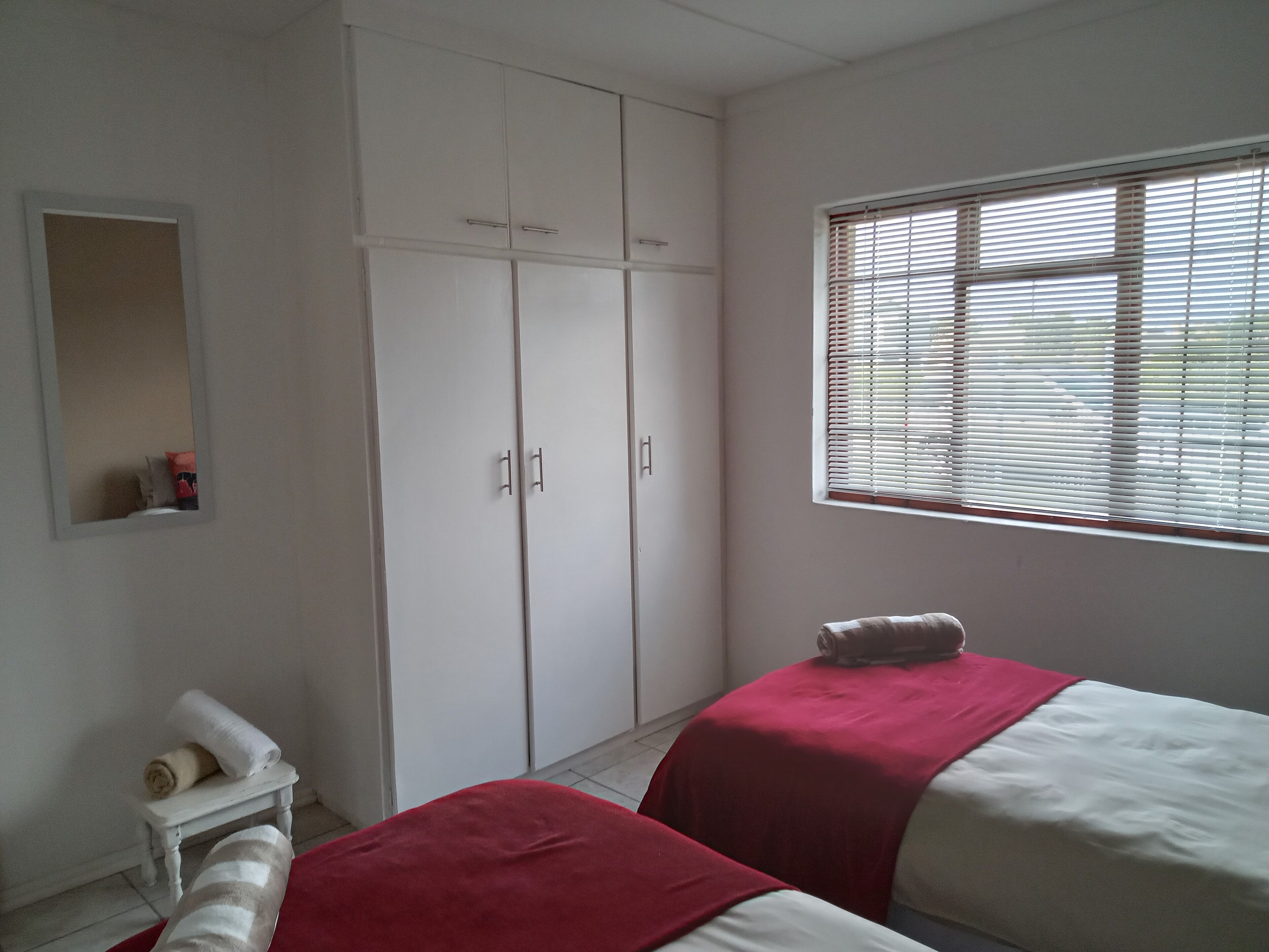 Ein Schlafzimmer mit zwei Betten, einem Kleiderschrank, einem kleinen Tisch mit einem Handtuch und einem Fenster mit Jalousien.
