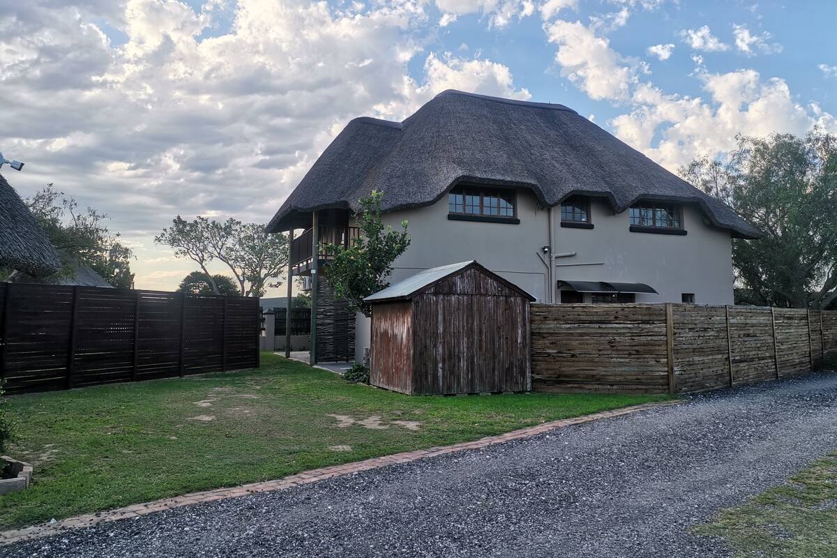 A house with a thatched roof, a wooden fence, and a gravel driveway.