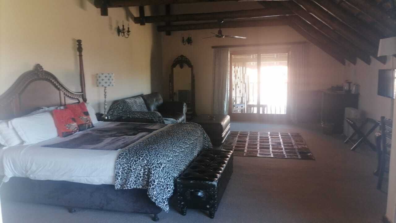 A bedroom with a bed, a bench, a mirror, and a door leading to another room.