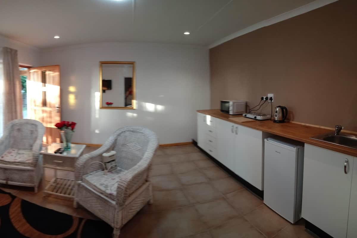 A compact living space with a kitchenette, two wicker chairs, a small table, and a patterned rug.
