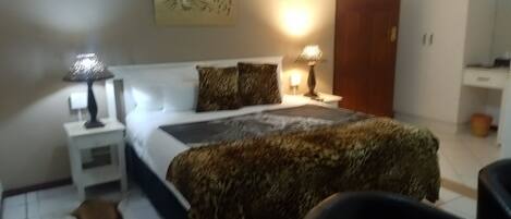 A bedroom with a bed, two bedside lamps, a leopard print throw, a mirror, and a wardrobe.