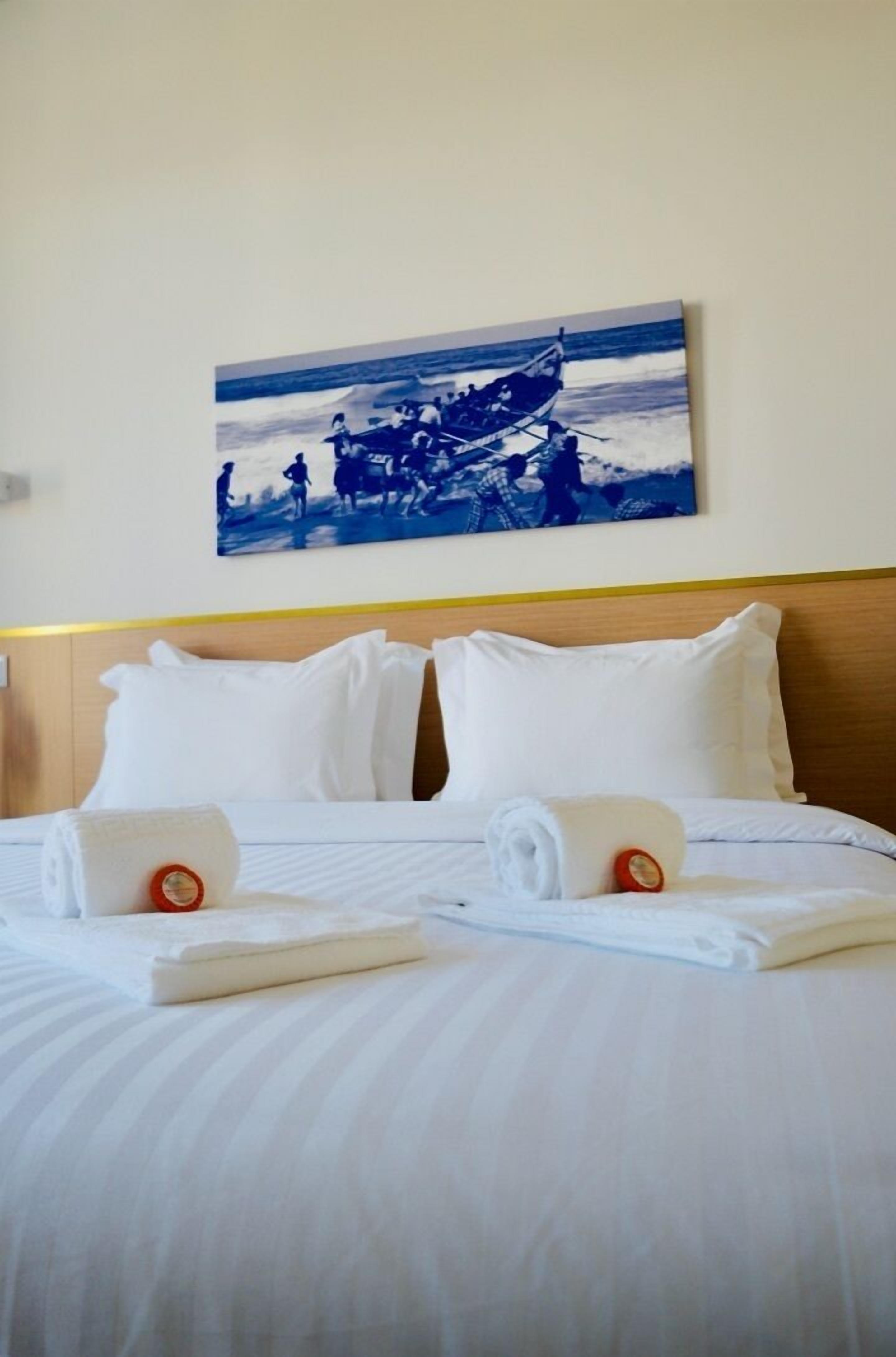 Une chambre d’hôtel avec un lit bien fait, une tête de lit et un tableau représentant un bateau accroché au mur.
