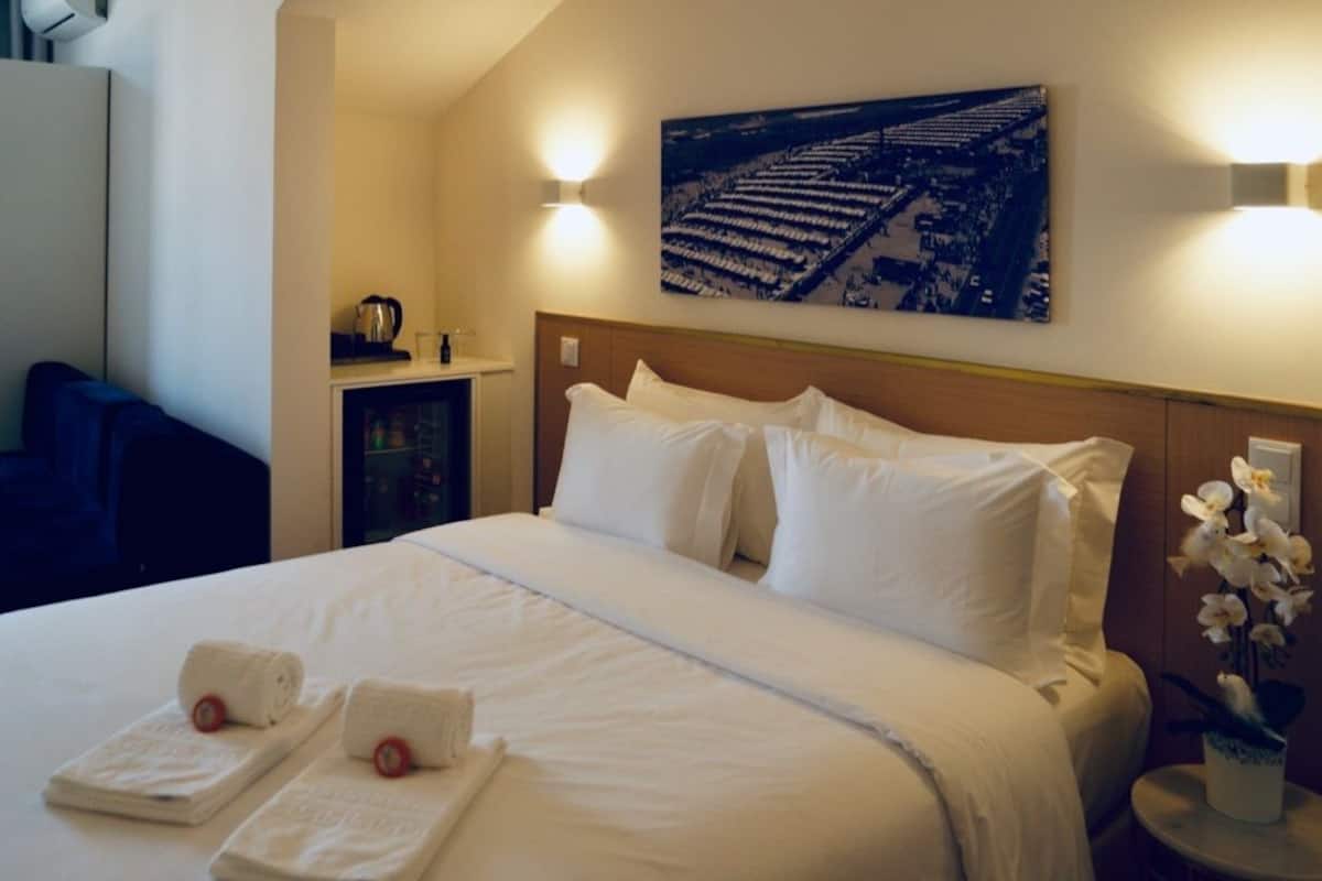 A hotel room with a neatly made bed, a headboard, a small table with a vase of flowers, and a wall-mounted picture.