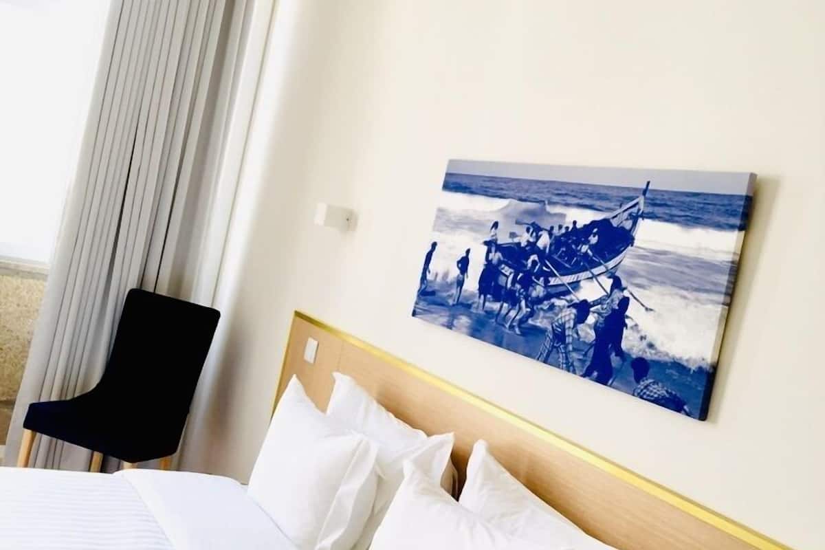 A hotel room with a bed, a chair, and a painting of a boat on the wall.