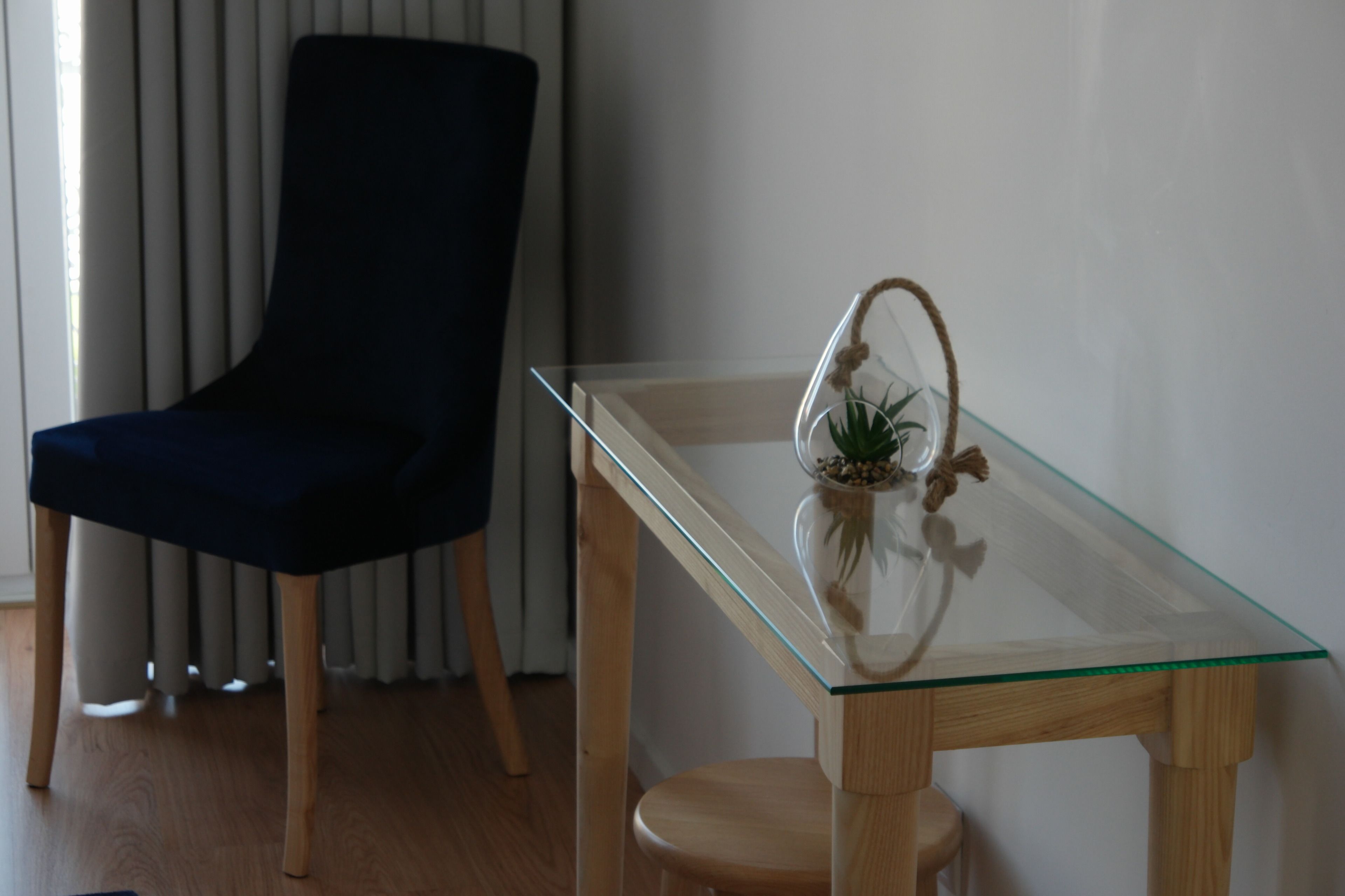 Een tafel met glazen blad, een kleine potplant, een donkerblauwe stoel en houten poten.