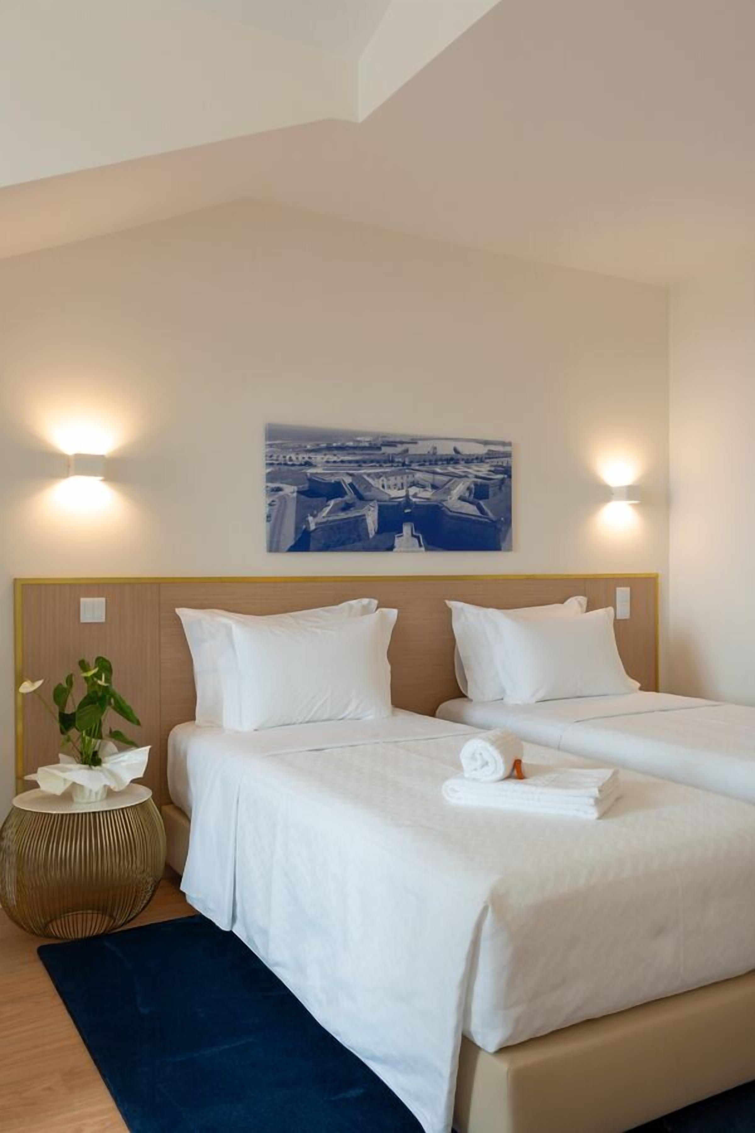 A hotel room with two beds, a cityscape painting, and a round side table with a plant.