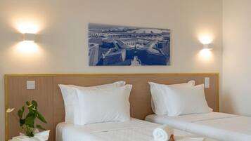 A hotel room with two beds, a cityscape painting, and a round side table with a plant.